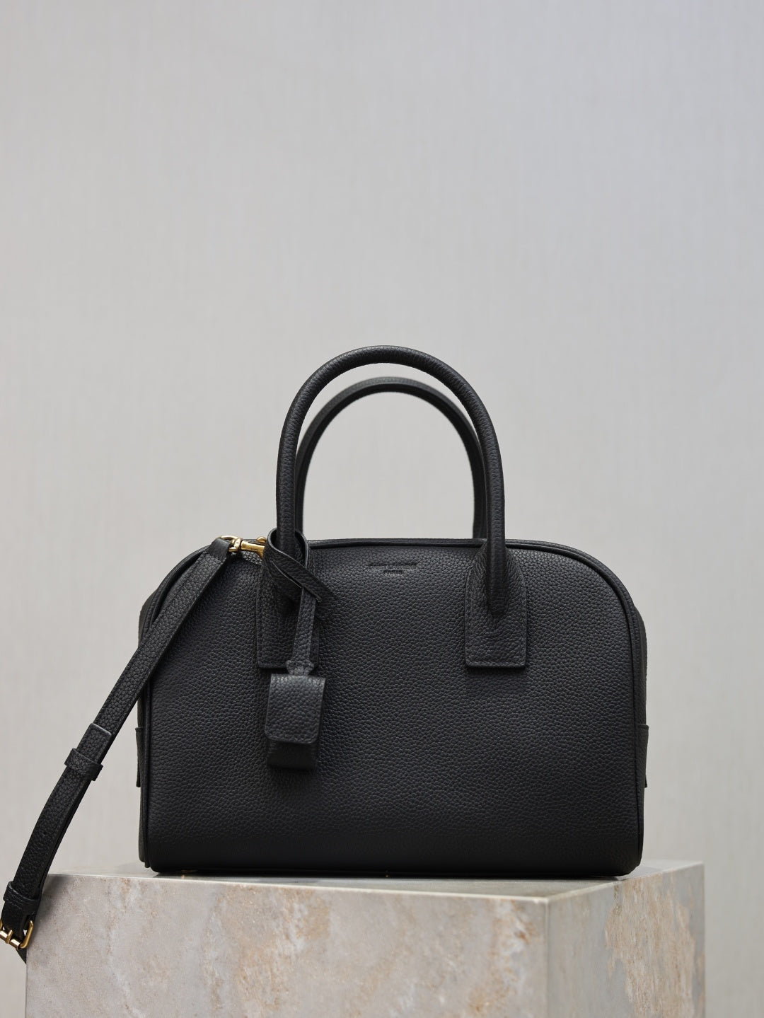 Black structured handbag with top handles, front strap detail, and crossbody strap