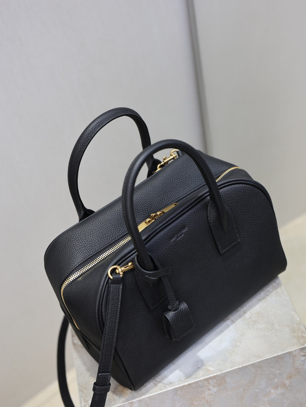 Black structured handbag with top handle, front zipper pocket, and crossbody strap
