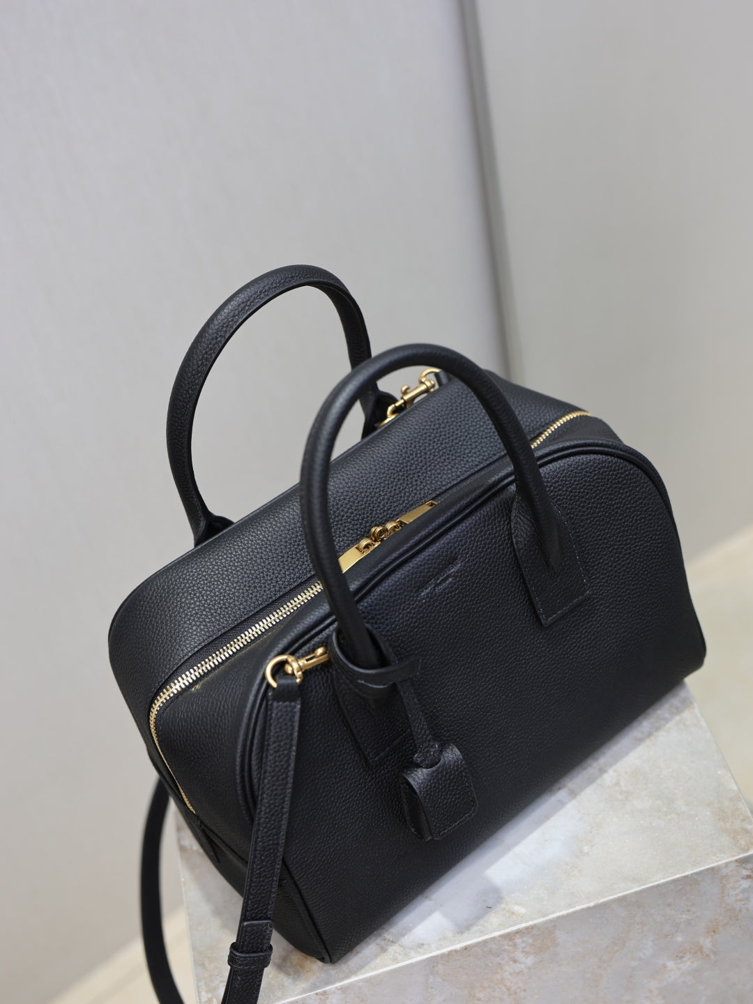 Black structured handbag with top handle, front zipper pocket, and crossbody strap