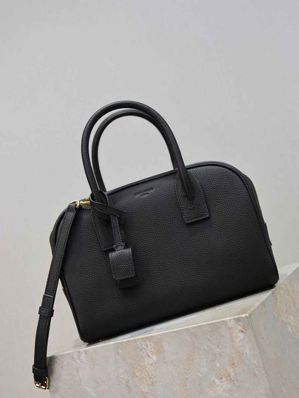 Black structured handbag with top handle, front strap detail, and adjustable shoulder strap