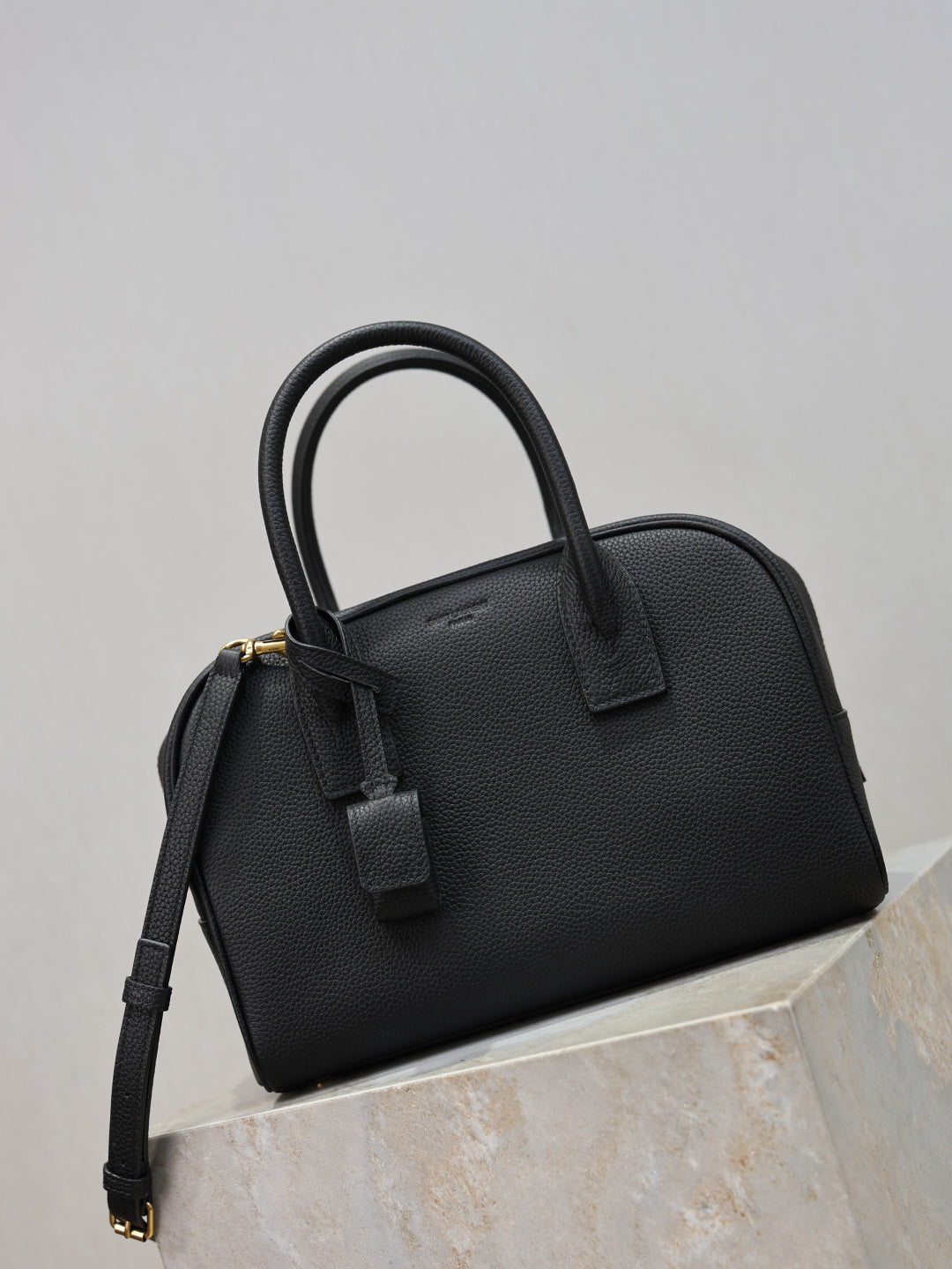 Black structured handbag with top handle, front strap detail, and adjustable shoulder strap