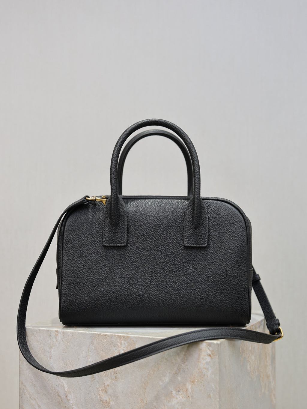 Black structured handbag with top handles and crossbody strap, front detail tab