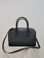 Black structured handbag with top handles and crossbody strap, front detail tab