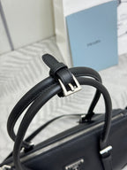 Prada handbag detail: dark leather strap and gold-tone buckle, textured top zipper.