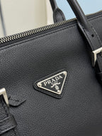 Prada handbag close-up: textured dark leather and metal logo plaque on front.