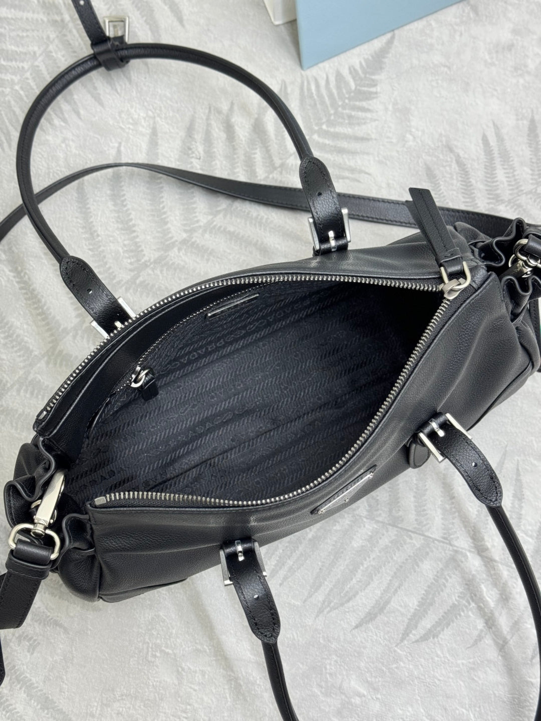 Prada handbag at an angle: dark leather, top zipper, shoulder strap, gold hardware.