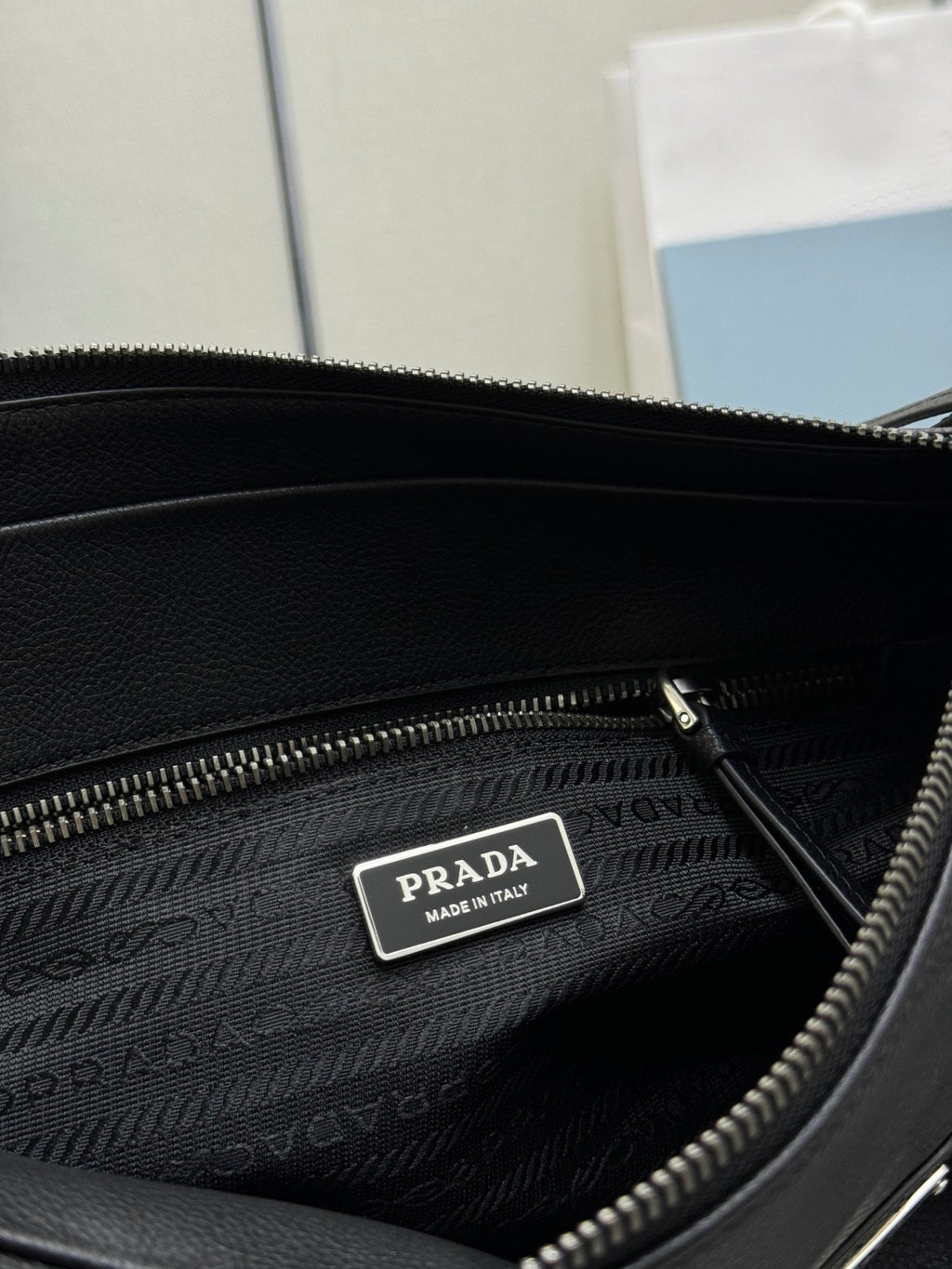 Prada handbag interior close-up: dark lining, zip pocket, metal logo tag.