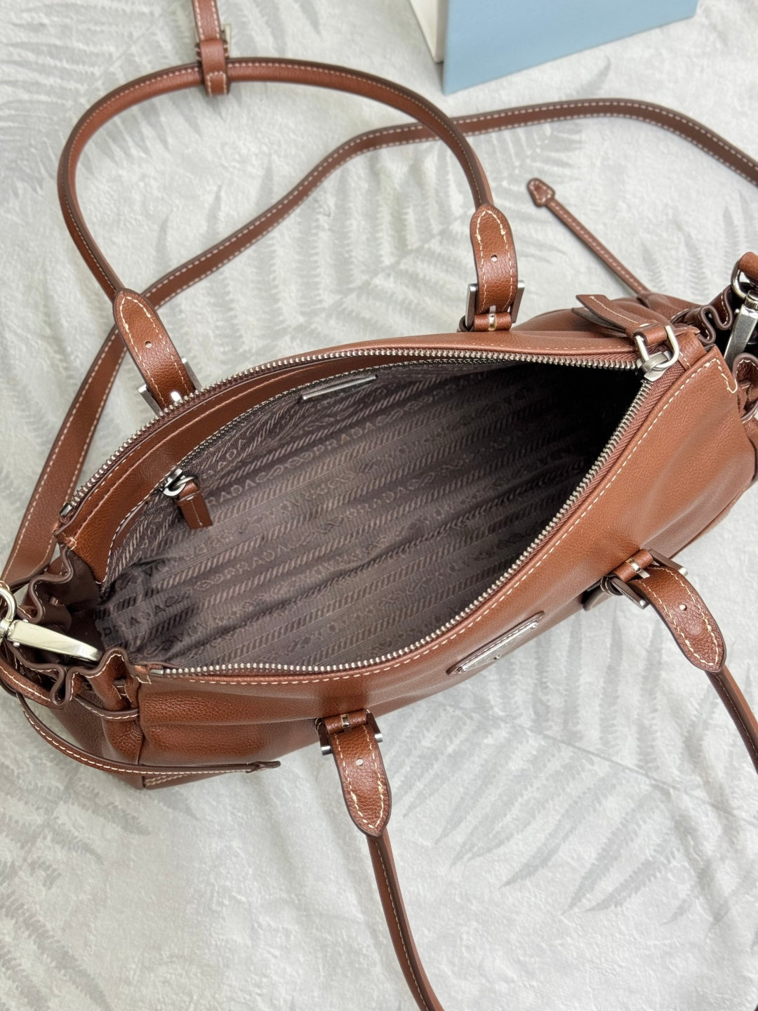 Brown Prada mini bag with zip top, patterned interior, and dual shoulder straps