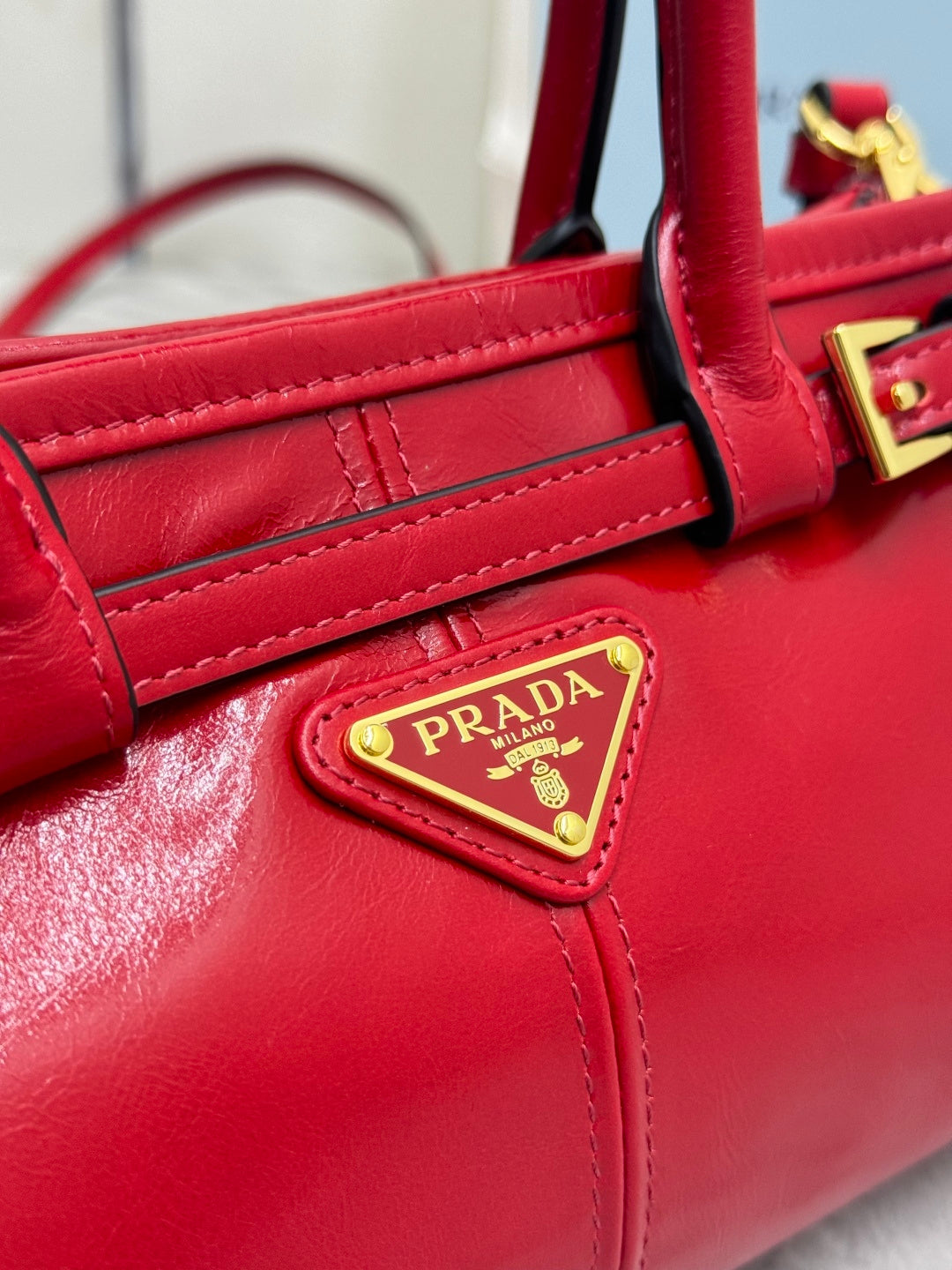 Red leather handbag front panel with stitched straps and gold logo plaque