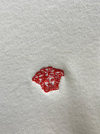 Off-white knit sweater detail: small red Medusa logo embroidery.