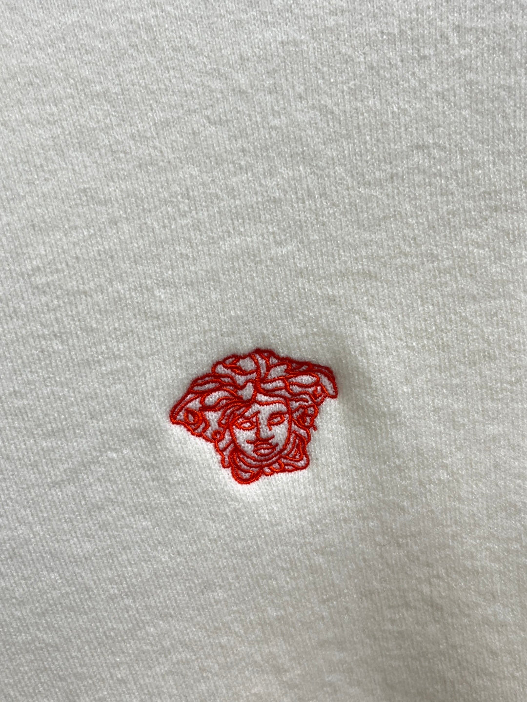 Off-white knit sweater detail: small red Medusa logo embroidery.