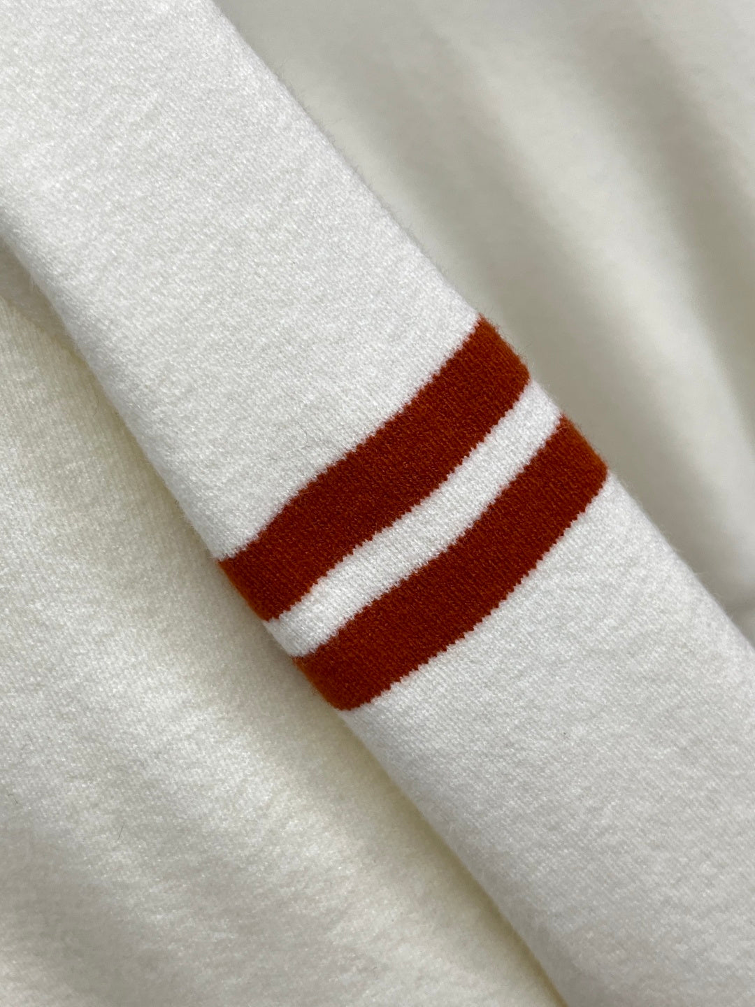 Off-white knit sweater sleeve cuff with red and white striped band.