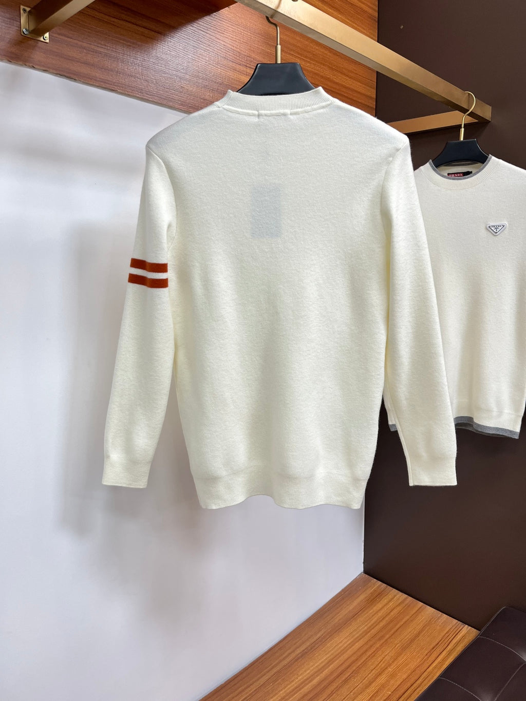 Off-white crewneck sweater with red logo and red-and-brown striped sleeve cuff.