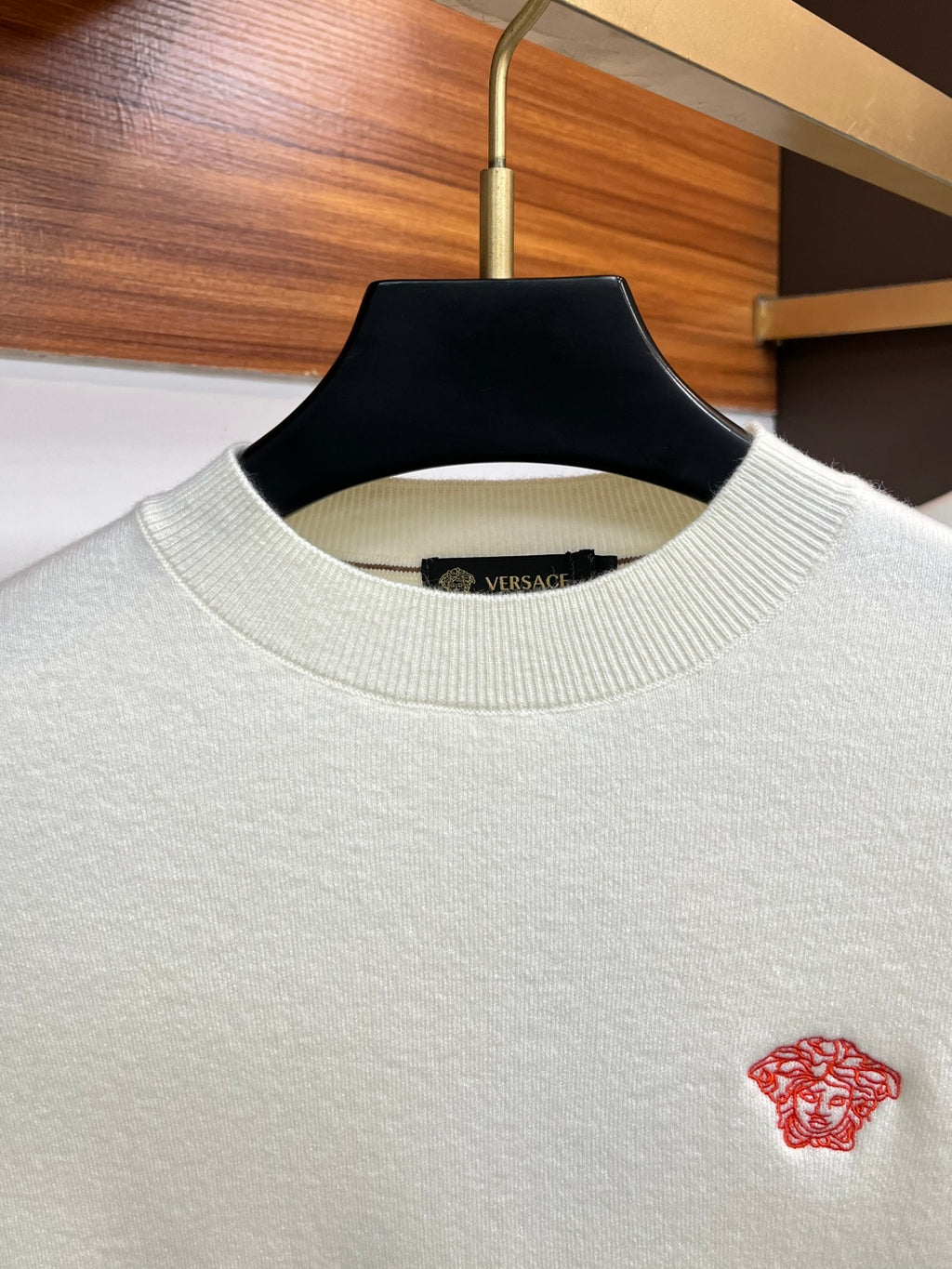 Off-white Versace knit sweater close-up with red Medusa logo at chest.