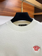 Off-white Versace knit sweater close-up with red Medusa logo at chest.