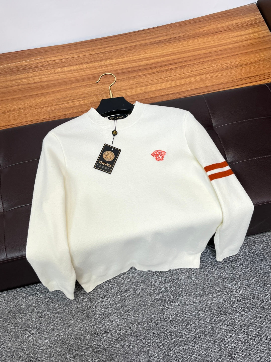 Off-white Versace crewneck sweater with red logo and striped sleeve on hanger.