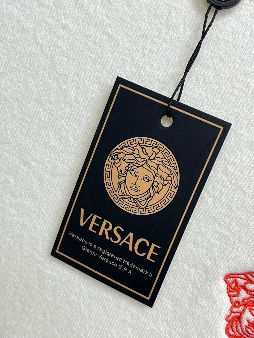 Off-white knit sweater with black Versace hangtag and circular Medusa design.