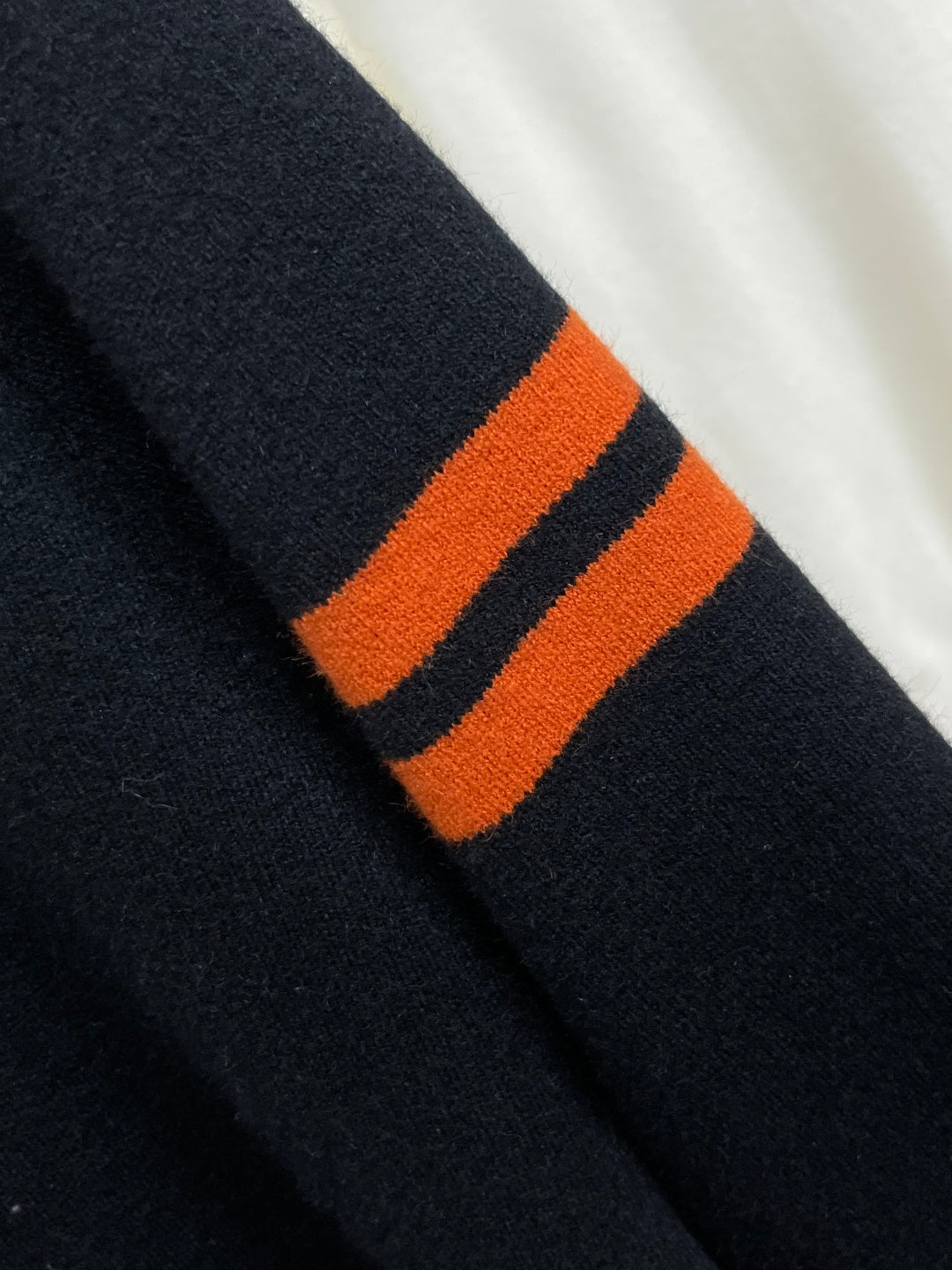 Black knit sweater sleeve with orange and dark stripe ribbed band