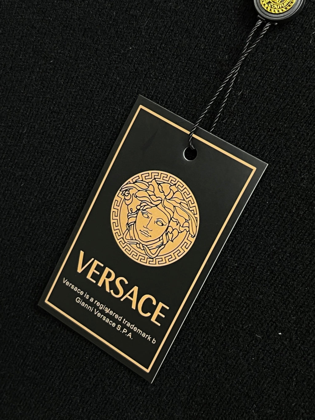 Versace brand neck tag on black knit sweater with gold outline logo graphic