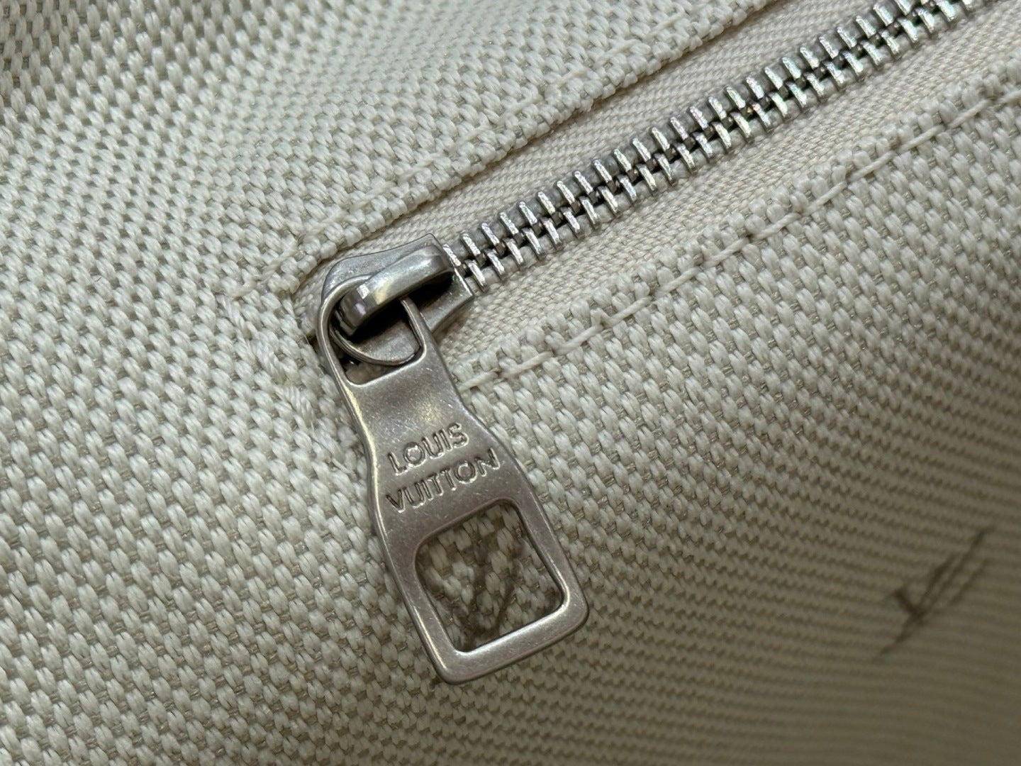 Beige Louis Vuitton bag zipper pull on textured canvas with monogram marks
