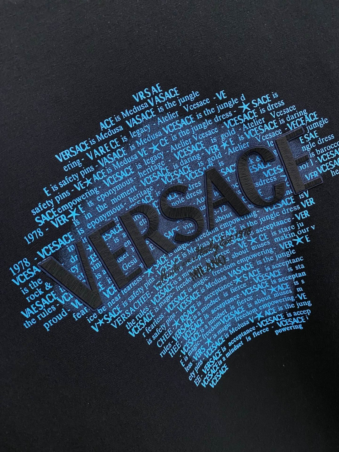 Blue Versace Medusa graphic and repeated text print on black sweatshirt front.