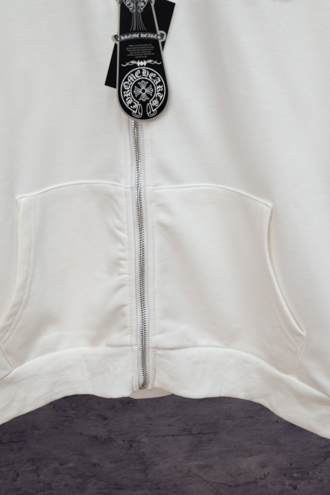 White zip-up hoodie front with center zipper, logo hood pocket, and charm pendant