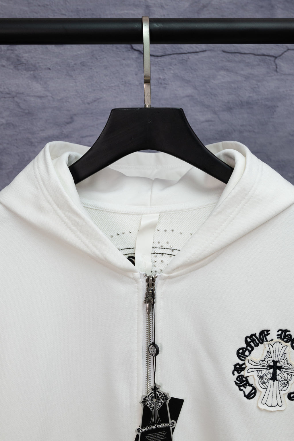 White long-sleeve zip hoodie close-up with hood, zipper, and hanging cross charm