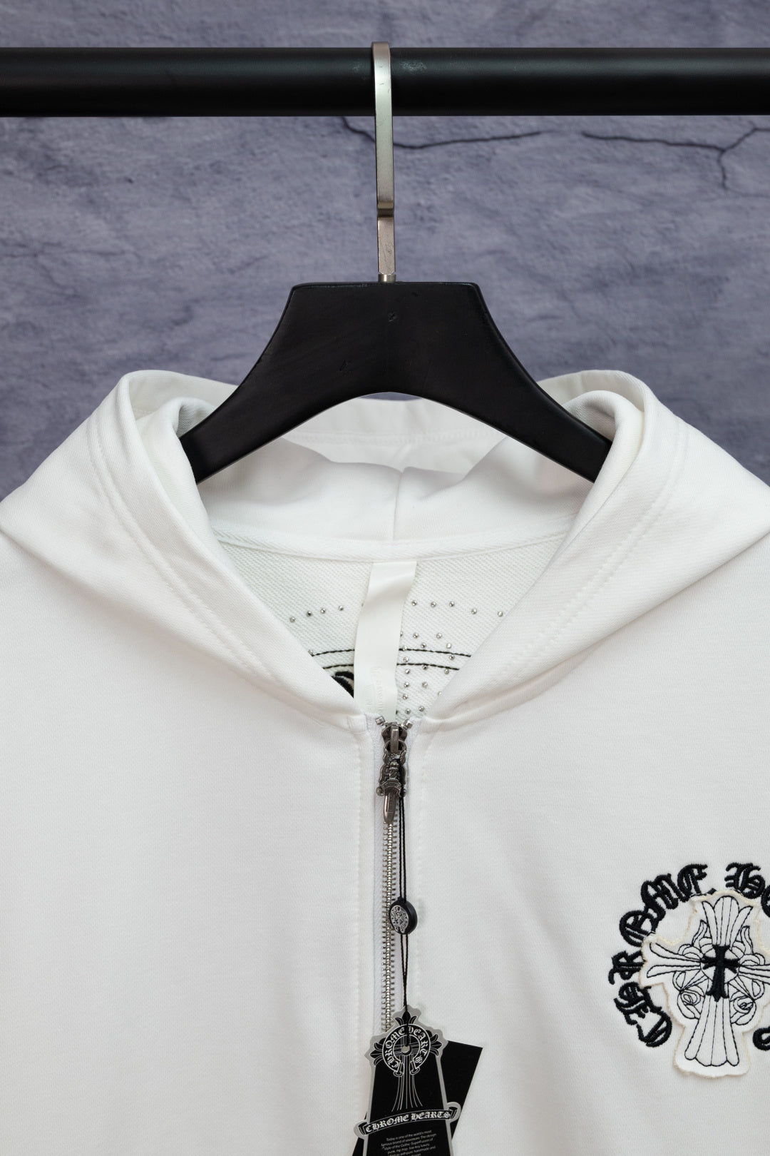 White long-sleeve zip hoodie close-up with hood, zipper, and hanging cross charm