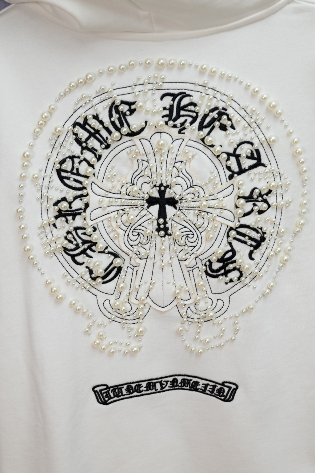 White hoodie back with round crest graphic, pearl trim, and arched lettering