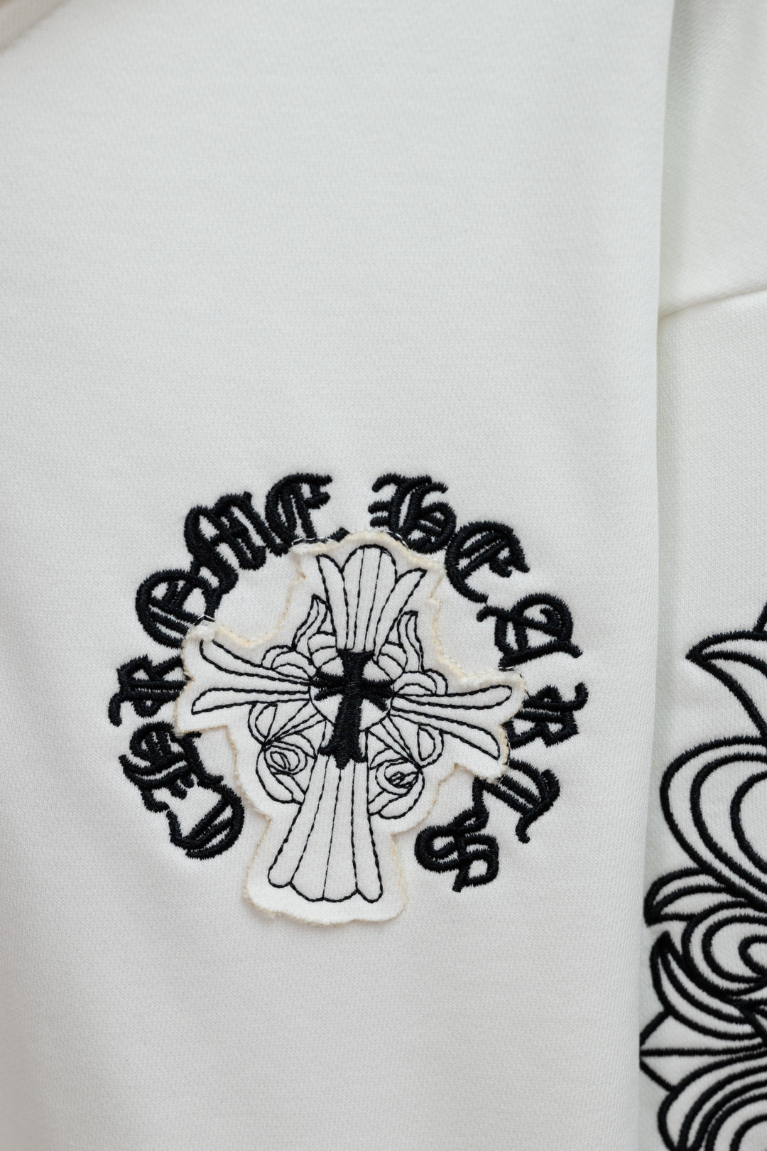 White hoodie sleeve with black cross and decorative lettering graphic