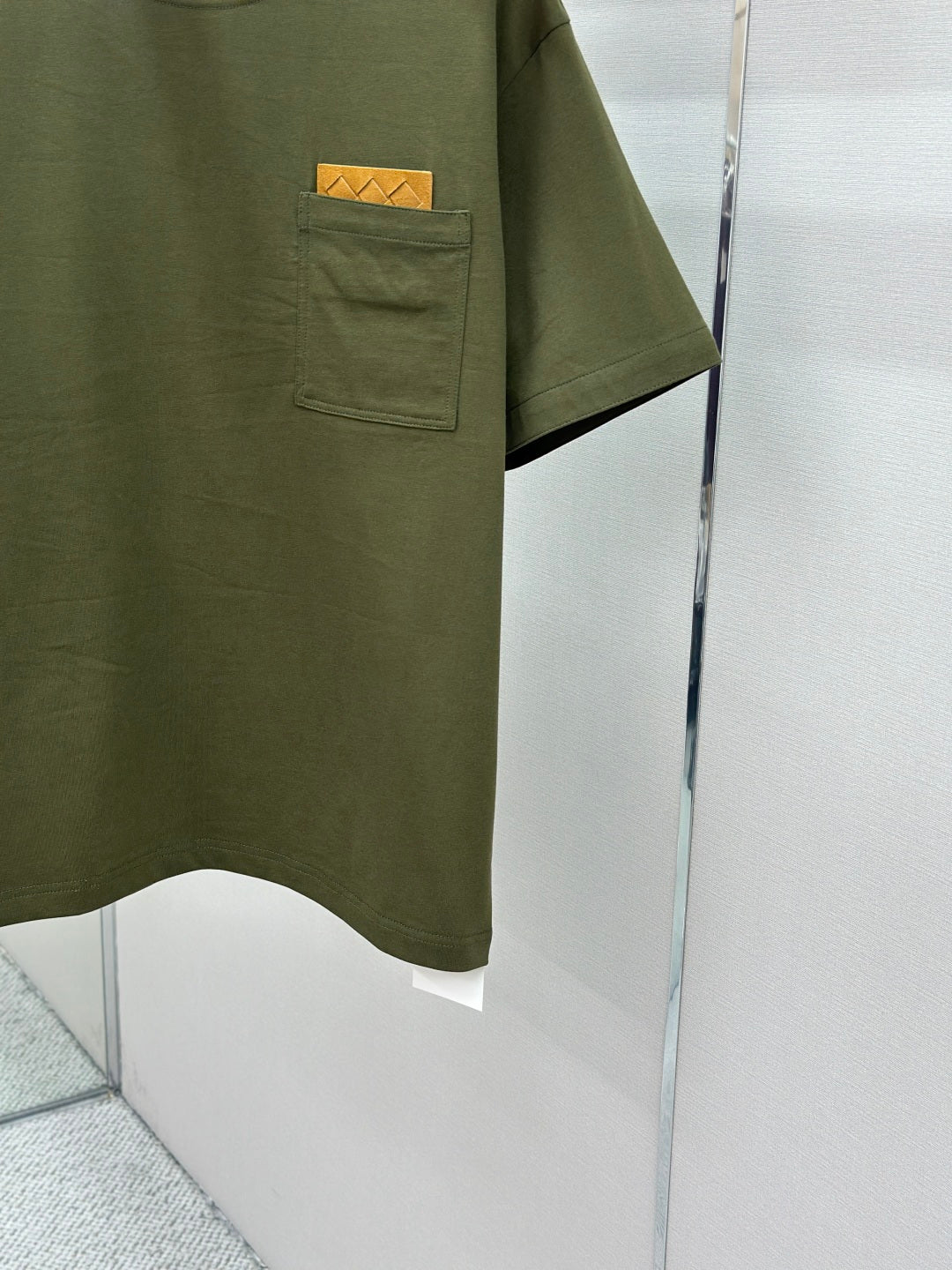 Olive green crew-neck T-shirt with chest pocket and logo patch, side view