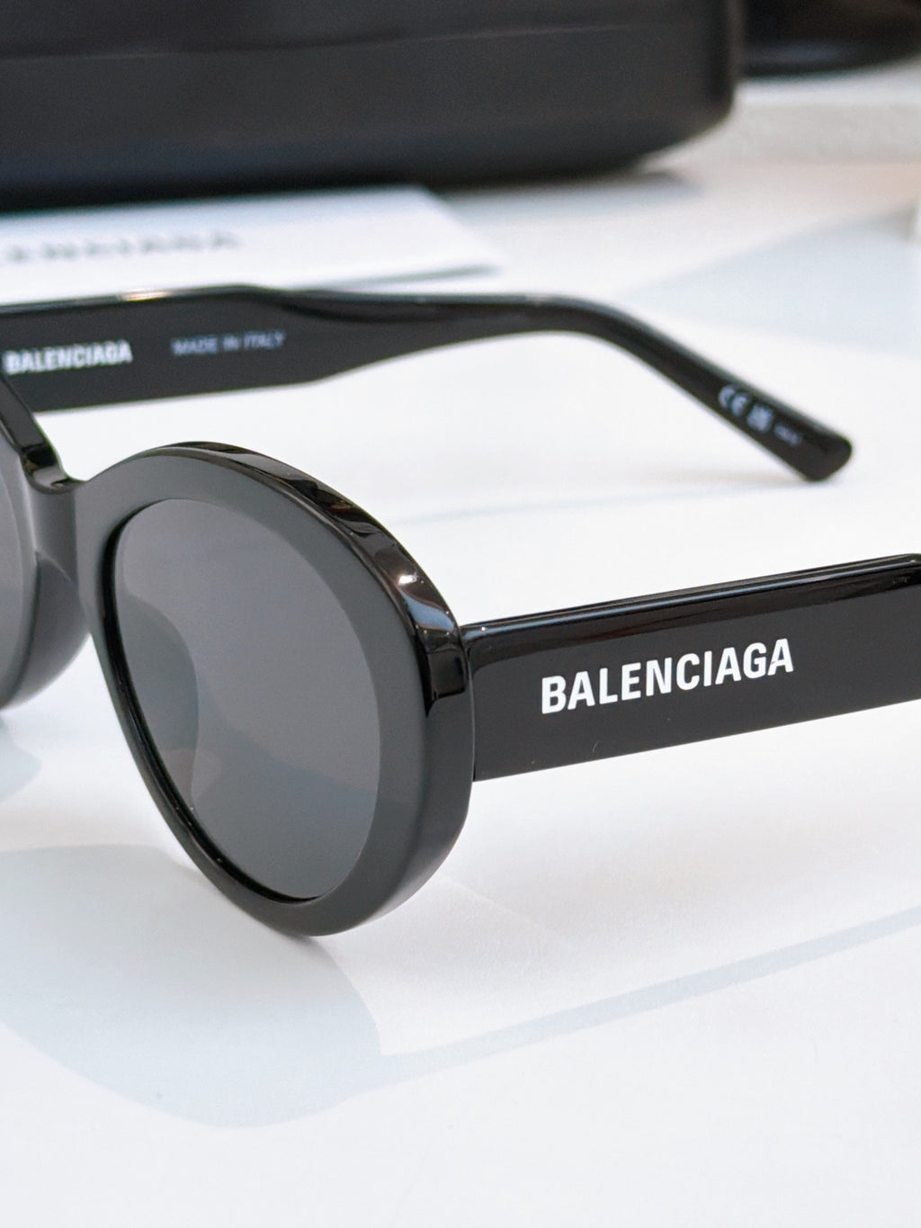 Black round sunglasses close-up with dark tinted lenses and brand text on arm.