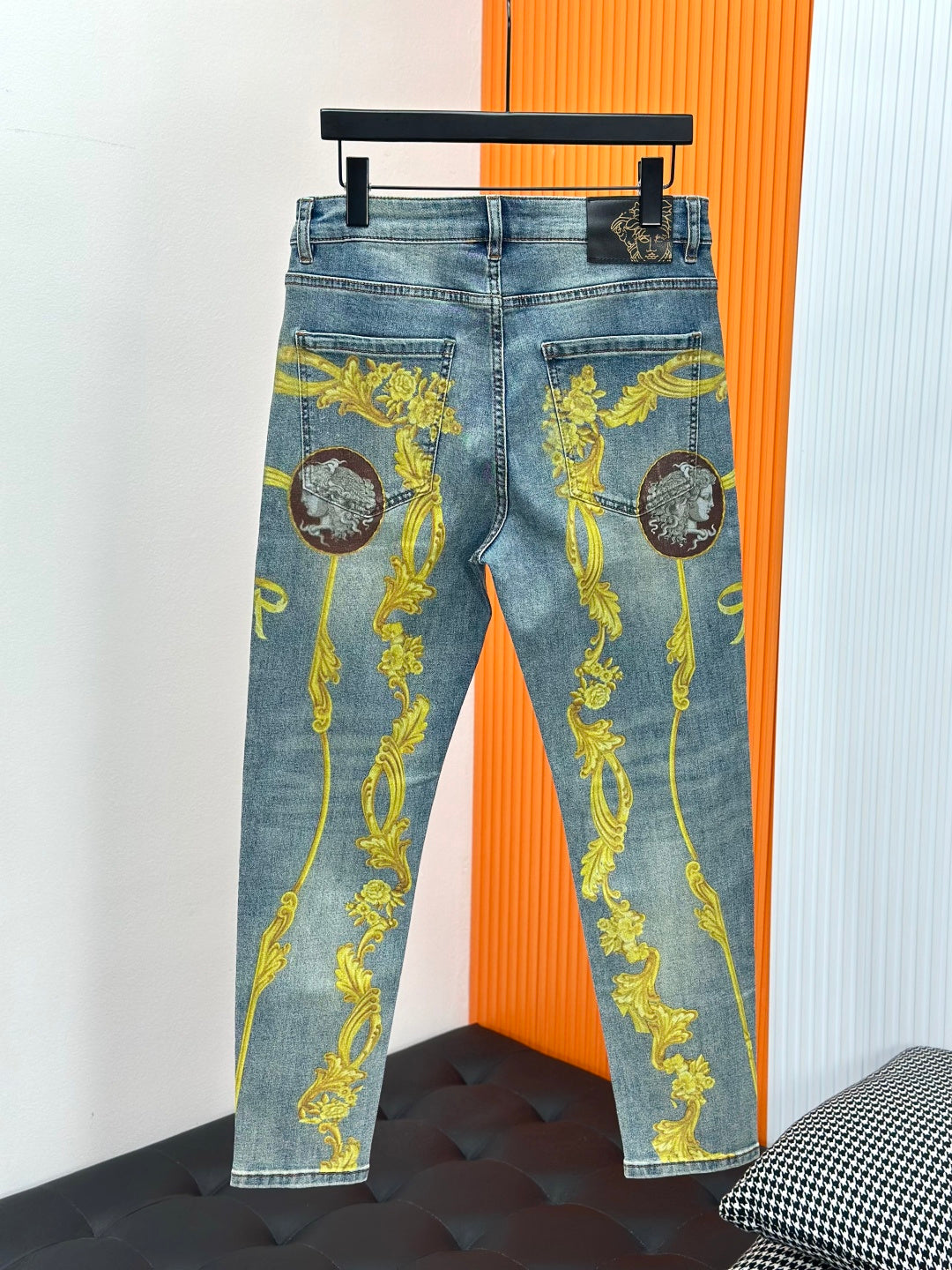 Light blue Versace jeans with gold baroque medallion ornament print, hanging on rack