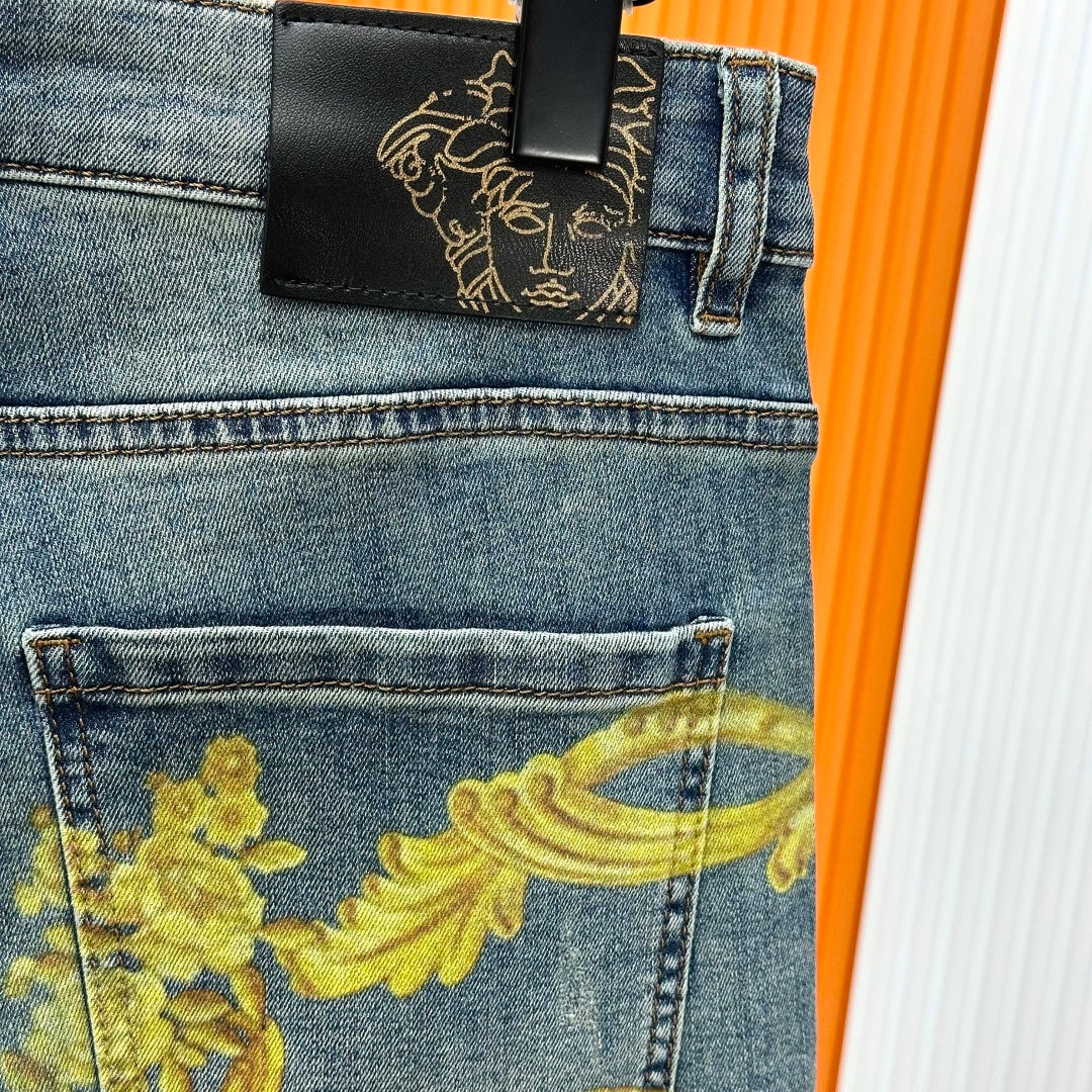 Blue denim jeans with black logo patch and gold baroque print detail on front pocket.