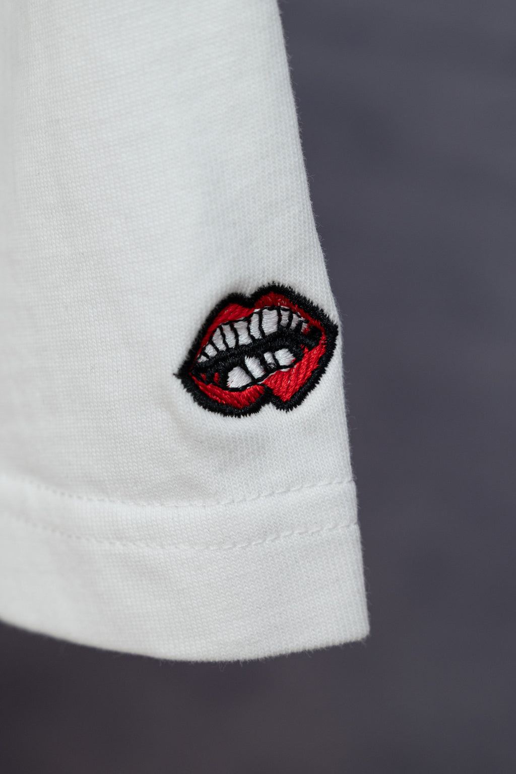 White T-shirt sleeve with red-and-black embroidered lip logo patch