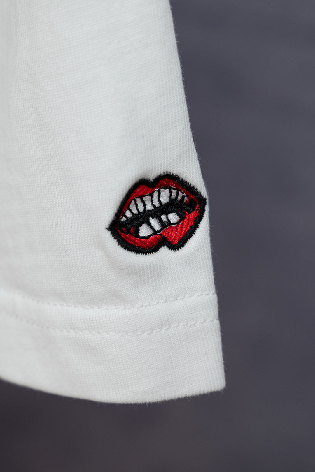 White T-shirt sleeve with red-and-black embroidered lip logo patch