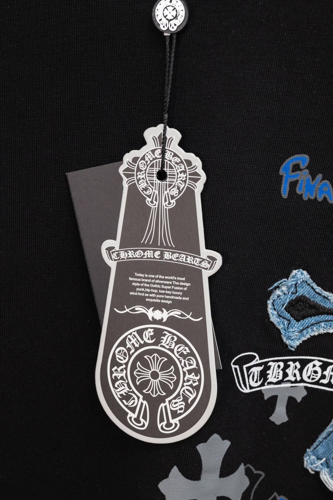 Black T-shirt close-up with white emblem hang tag and blue cross graphic