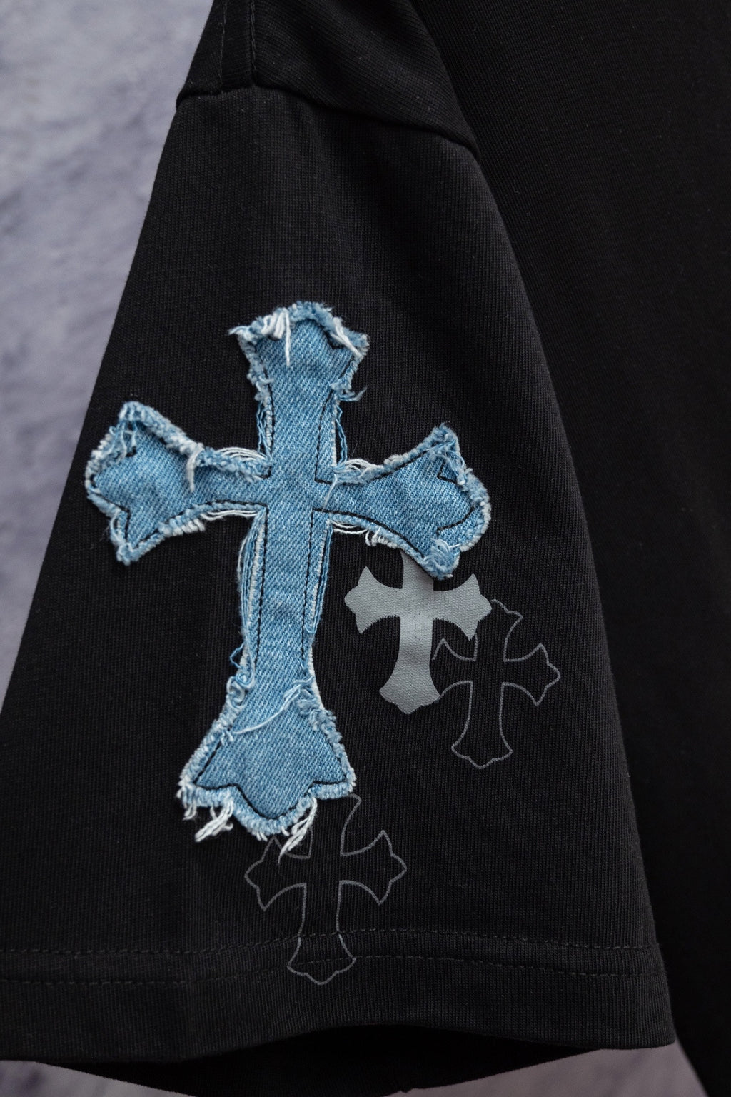Black T-shirt sleeve detail with large blue cross embroidery