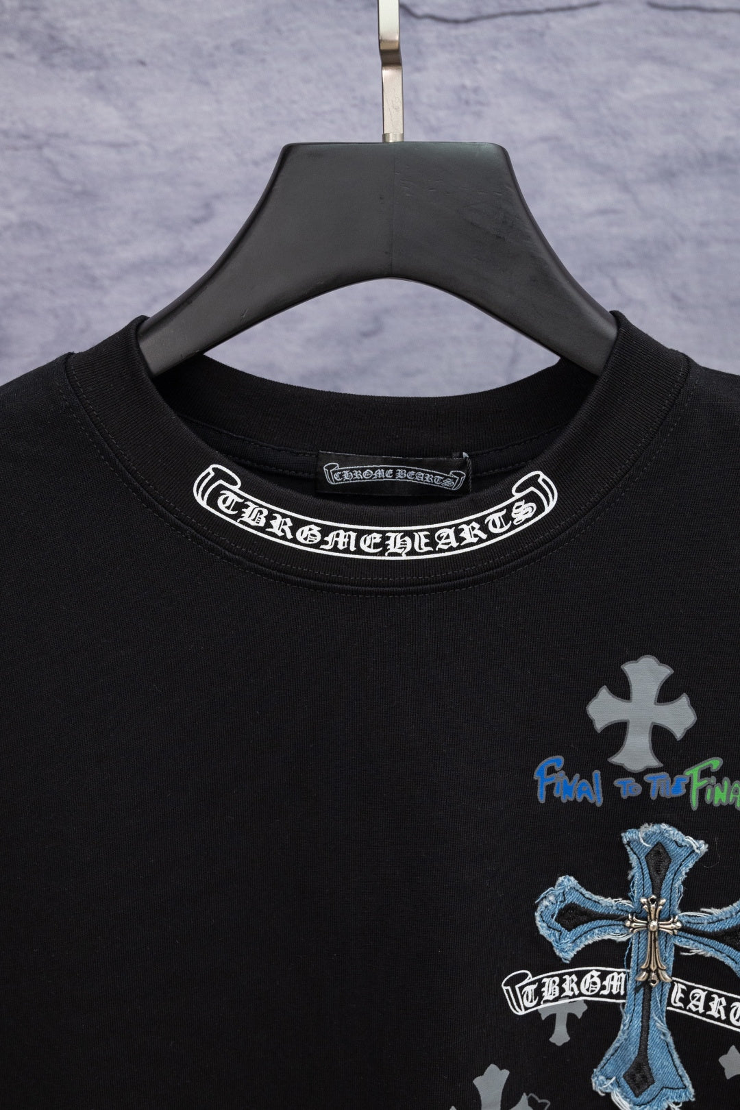 Black T-shirt neckline with white circular text graphic, blue and gray chest logo