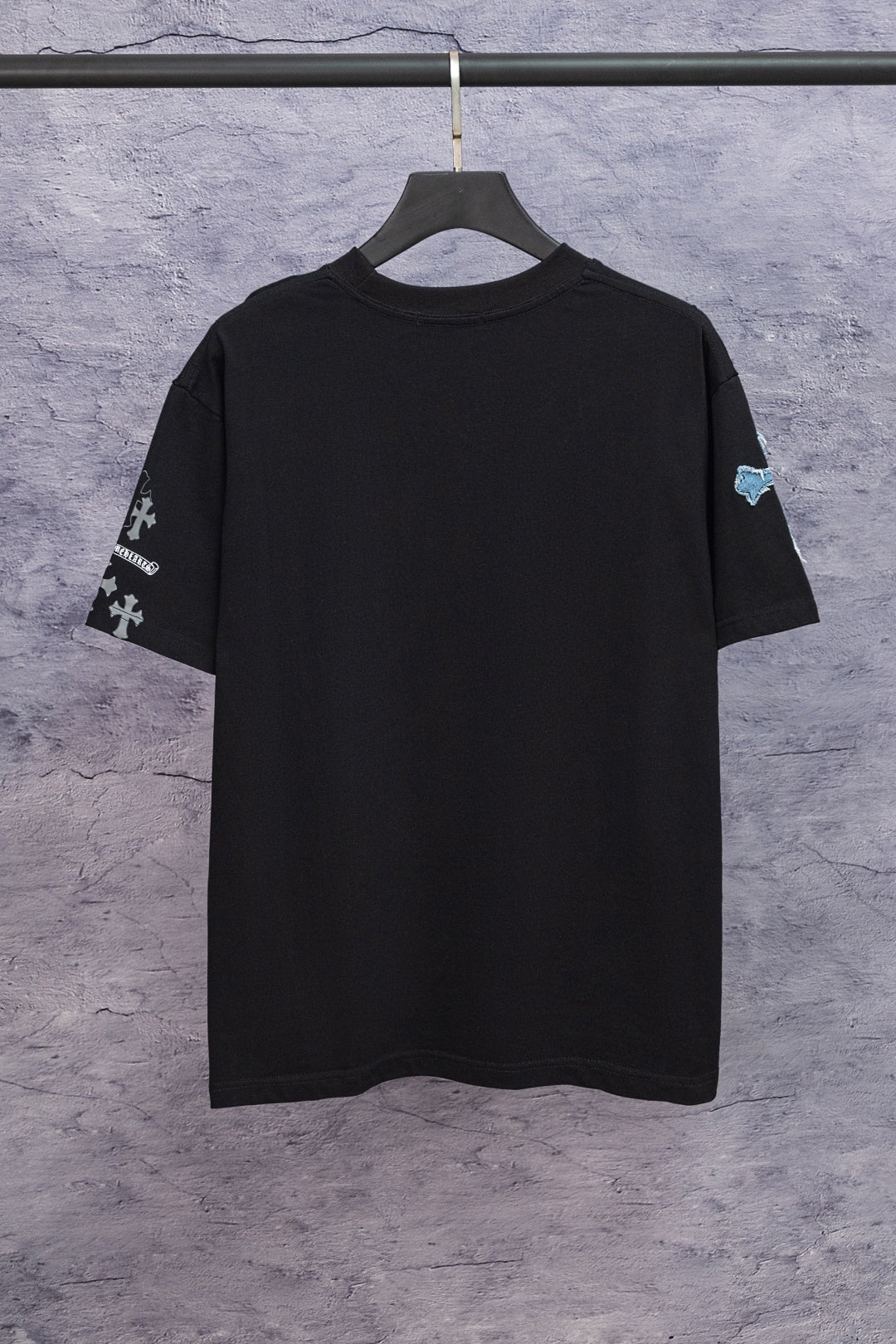 Black graphic T-shirt back view with blue sleeve emblem, hanging on a black hanger