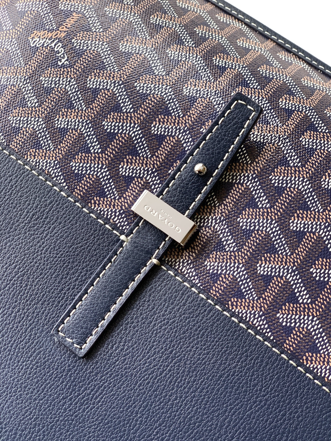 Leather tab and snap detail on navy monogram bag with stitched trim