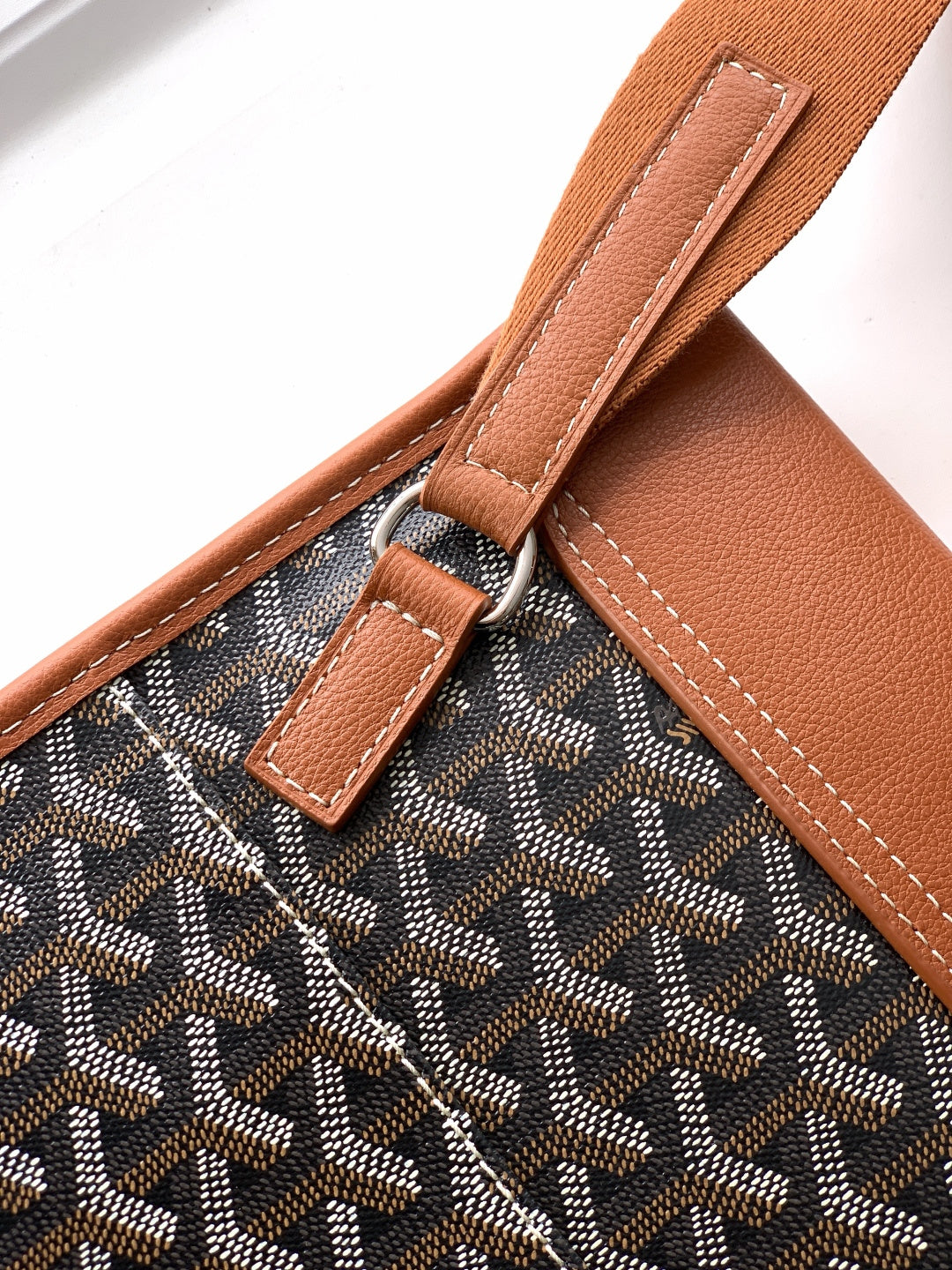 Goyard bag close-up of tan strap attachment with metal ring and stitching.