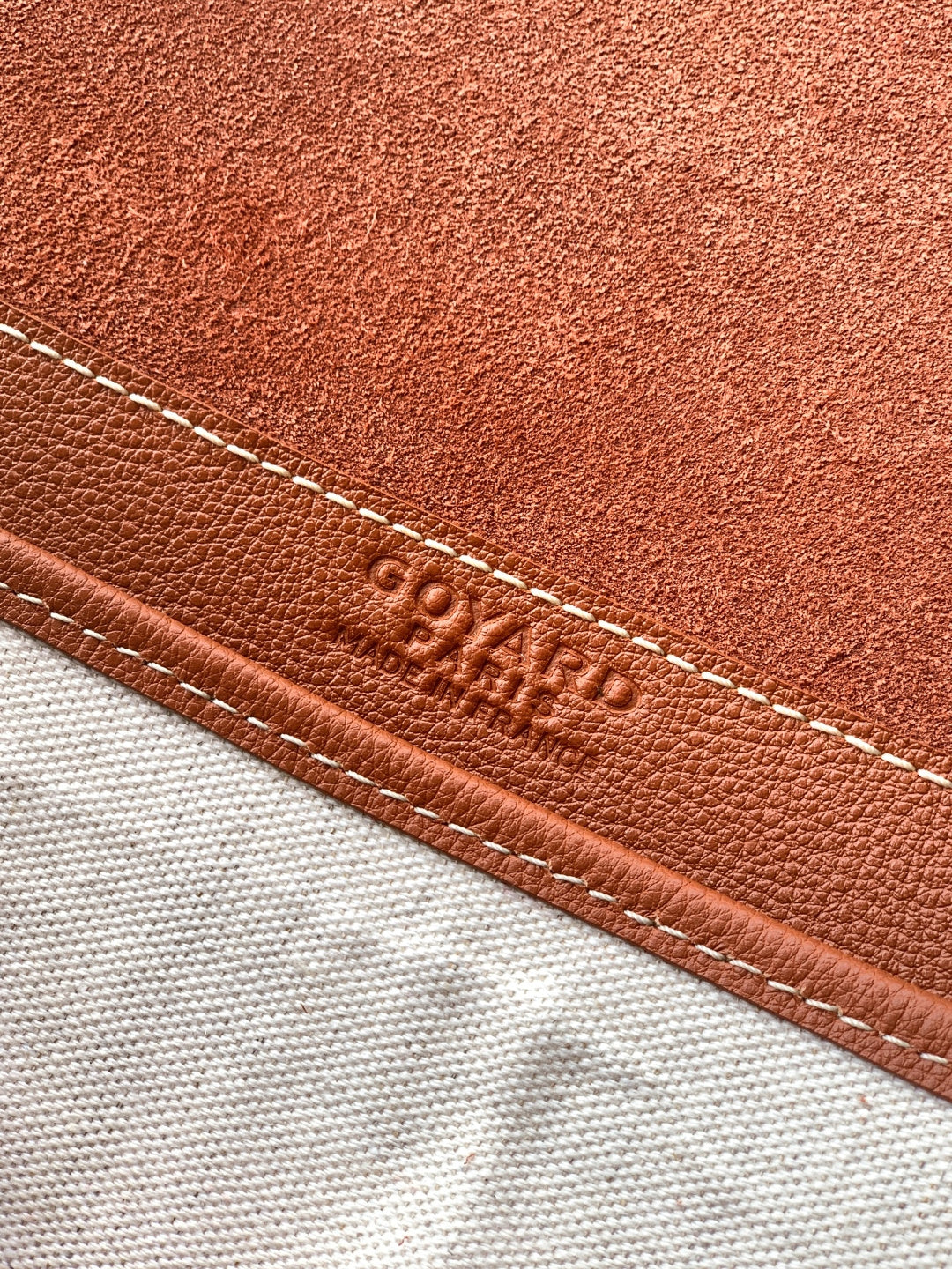 Goyard leather trim close-up with embossed logo and contrast stitching.