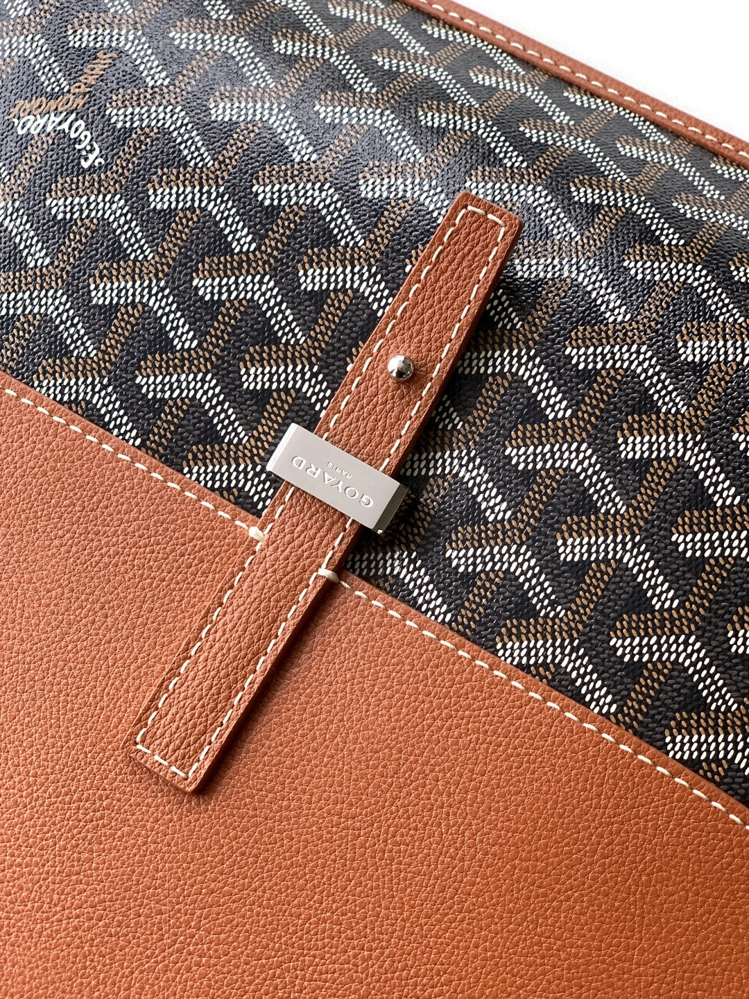 Goyard crossbody bag close-up of tan leather patch and stitched edge.