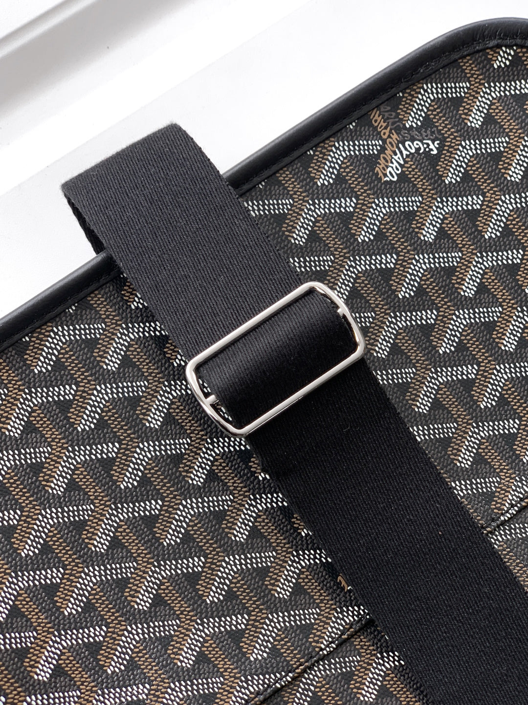 Goyard bag strap detail: black webbing with metal buckle over gray patterned panel