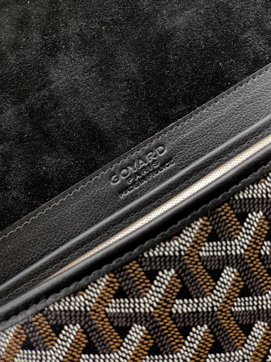 Goyard bag logo detail on black leather trim with gray patterned fabric beside it