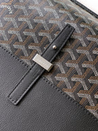 Goyard bag detail: gray patterned fabric with black leather panel and stitched tab