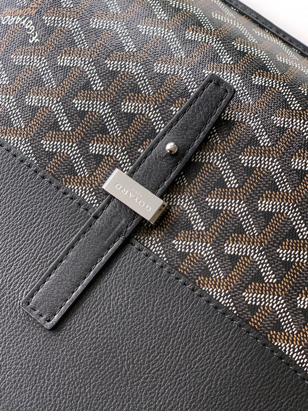 Goyard bag detail: gray patterned fabric with black leather panel and stitched tab