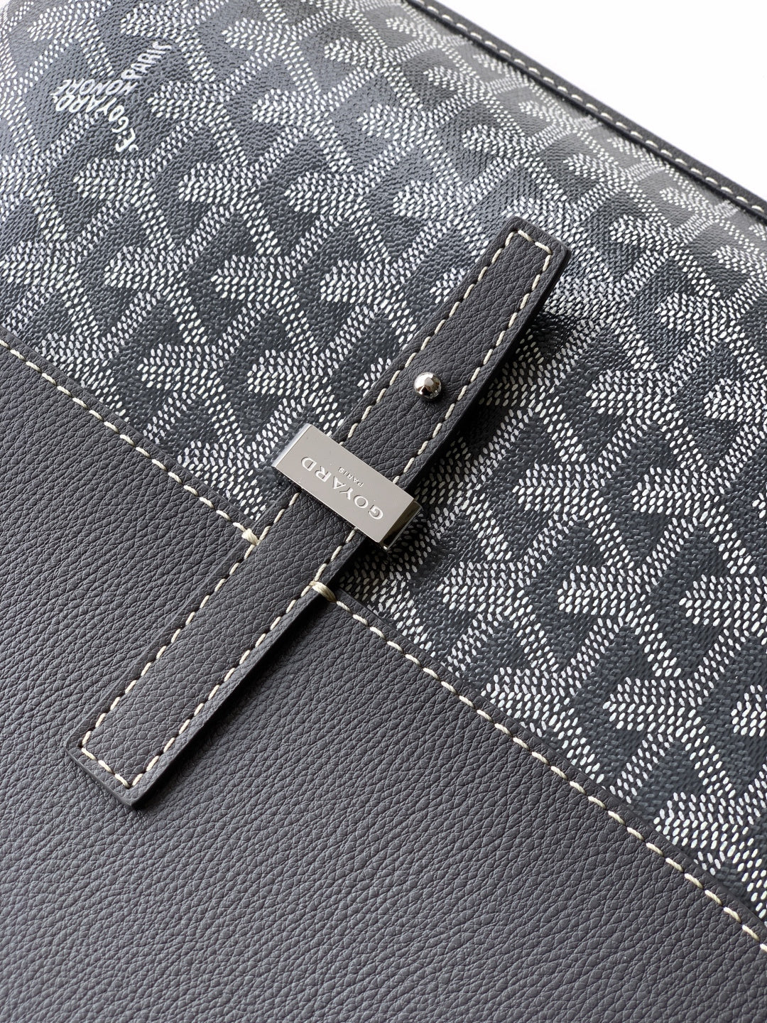 Goyard bag close-up of dark patterned flap with stitched details and metal clasp