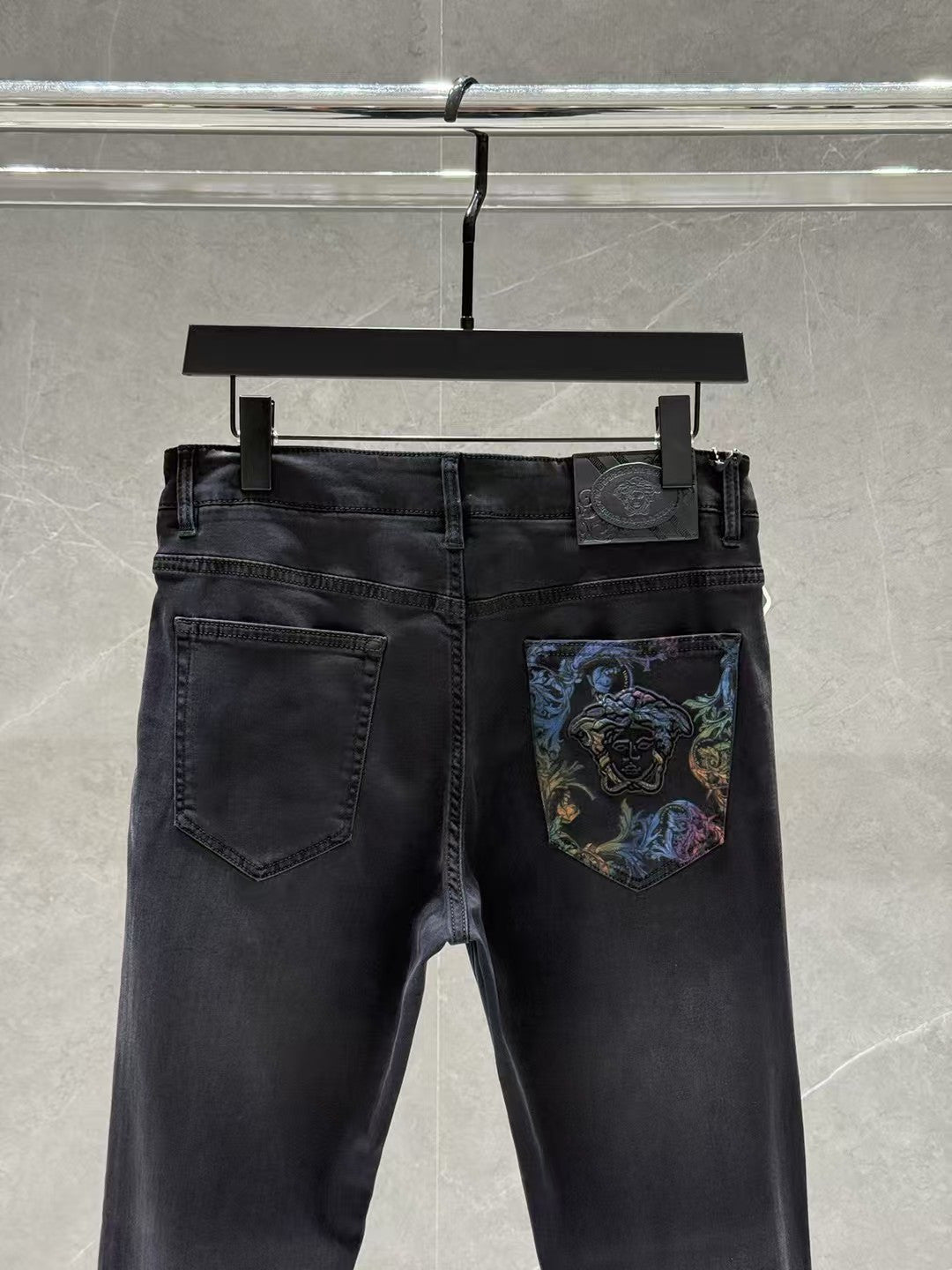 Dark denim jeans with belt loops and a colorful graphic patch on the front right pocket.